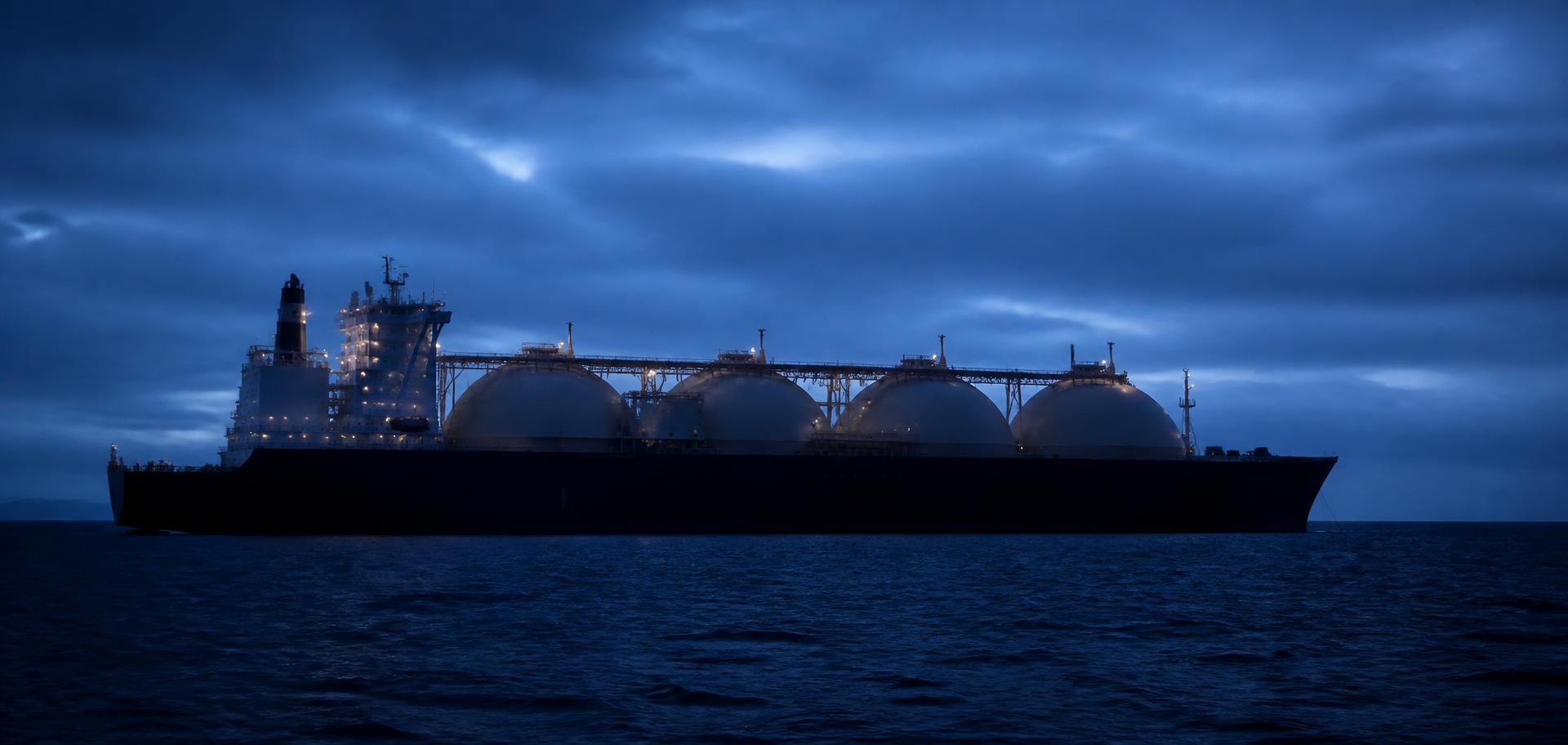 An LNG carrier at sea under an overcast blue-hour sky
